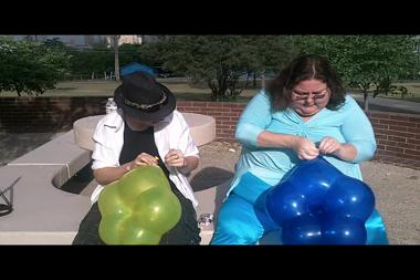 2 Blow Up Interesting Star Shaped Balloons Out Side - The are trying out some new star shaped ballons for the first time and they have great fun blowing them to show you how big they get what shape they finally take and what naughty things they can do with them this a cute bi guy and a very big woman she does pop hers by sitting on it !