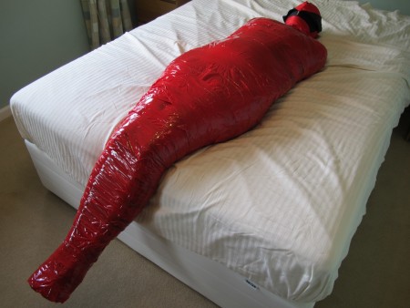 Karina Is Mummified In Red Packing Tape - In this clip we use red packing tape to totally mummify karina.  The red tape differs from the thin brown tape that we all use to fasten parcels only in its colour.  Thin and with an incredible ability to stick itself back to its roll, packing tape is very difficult from which to get free.
karina starts off the mummification process on herself by wearing tights to protect her skin from the excessive tackiness of the tape's glue.  Then she self-wraps her legs until she can wrap no further.
watch with us as we film karina disappearing under a layer of the red tape.  Her feet and toes are almost the last to disappear, followed, at last, by a red and black hood.
by the end of the process karina can barely move any part of her body, except her toes!