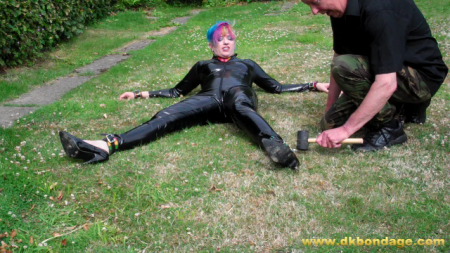 Mog Is Pegged Out In The Garden - Mog is looking stunning in her black, pvc, skin-tight catsuit and multi-coloured leather collar and cuffs.  We decide a sun-bathing session is what she needs and she agrees but we obviously did not agree how this was to be achieved.

mog is spreadeagled on the rear lawn of the garden using tent pegs.  We foolishly encourage her to escape thinking we have her pinned down.  Buy the clip to see what she does!

the final phase sees mog being double-pegged into the lawn with each peg driven deeply into the turf!

will she escape from this?